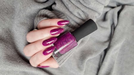 Woman hand with long nails manicure and pink fuchsia bottle with nail polishの写真素材