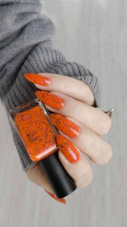 Woman hand with long nails and orange ginger manicure holds a bottle of nail polish