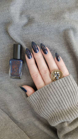 Female hand with long nails and blue manicure with bottles of nail polish