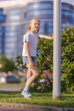 Blonde girl dancing, jumping, doing acrobatics and posing, in the city against the backdrop of buildings on a sunny dayの写真素材