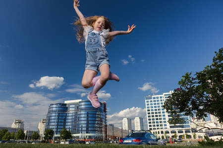 Blonde girl dancing, jumping, doing acrobatics and posing, in the city against the backdrop of buildings on a sunny dayの写真素材