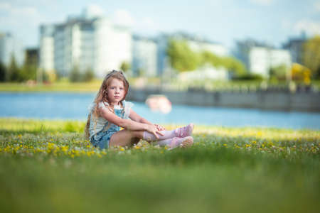Blonde girl dancing, jumping, doing acrobatics and posing, in a city park on green grass near a lake on a sunny dayの写真素材