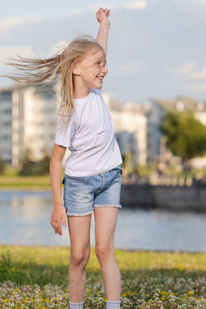 Blonde girl dancing, jumping, doing acrobatics and posing, in a city park on green grass near a lake on a sunny dayの写真素材