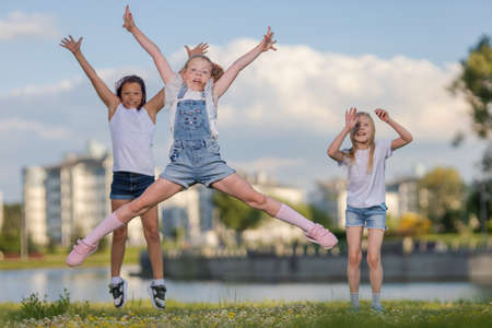 Children girls friends run, jump and pose near a lake in a city park on a sunny day