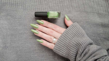 Woman's hands with long nails and a green manicure holds a bottle of nail polishの写真素材