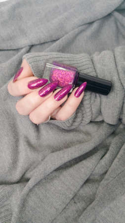 Woman's hands with long nails and a bottle of purple lilac color nail polishの写真素材