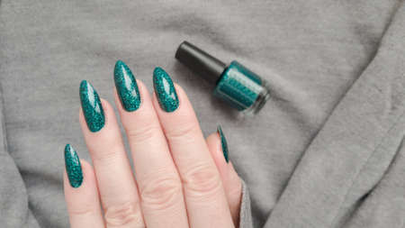 Woman's hands with long nails and a green manicure holds a bottle of nail polish