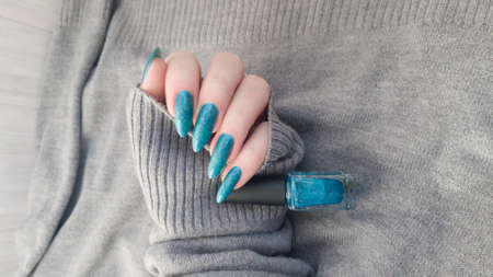 Woman's hand with long nails and turquoise blue manicure with bottles of nail polishの写真素材