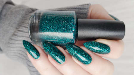 Woman's hands with long nails and a green manicure holds a bottle of nail polish