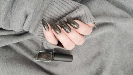Woman's hands with long nails and black manicure with bottles of nail polish
