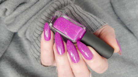 Woman hand with long nails manicure and pink fuchsia bottle with nail polishの写真素材