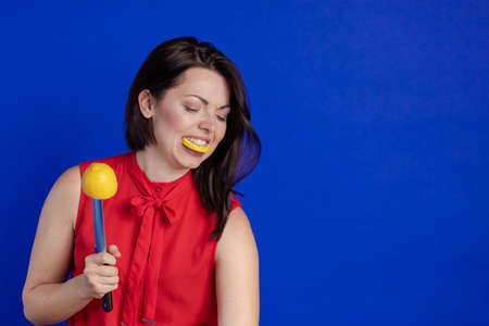 Emotional actress woman in a red blouse posing with a knife and lemon fruit in her hands on a blue backgroundの写真素材