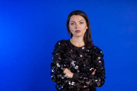Emotional young girl in a black shiny sweater posing on a blue background