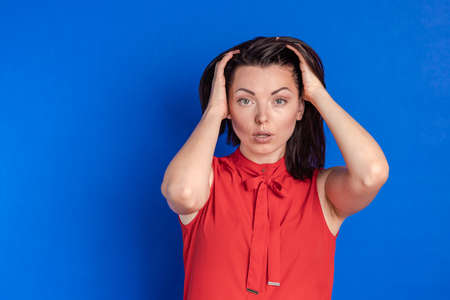Emotional actress young woman in a red blouse posing on a blue background