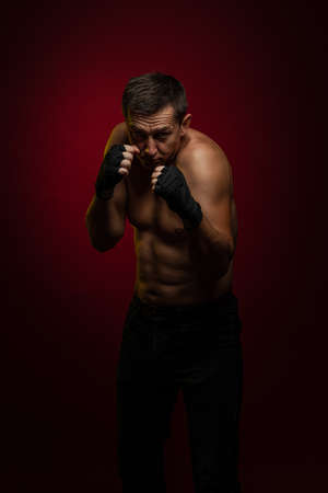 Male athlete boxer with gloves in his hands posing against a dark red backgroundの写真素材