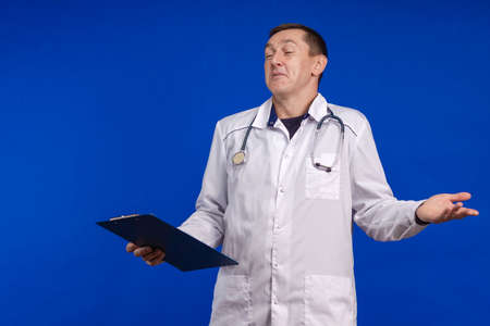 emotional adult male doctor in a white coat posing on a blue background