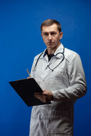 emotional adult male doctor in a white coat posing on a blue backgroundの写真素材