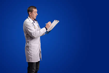 emotional adult male doctor in a white coat posing on a blue background