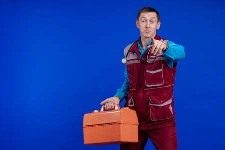 Ambulance doctor man in a medical uniform and with a box in his hands posing on a blue background