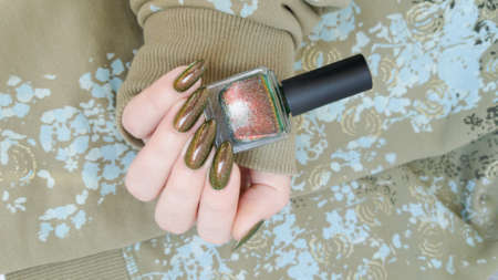 Female hand with long nails and a green manicure holds a bottle of nail polish