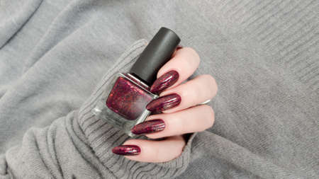 Female hand with long nails and a bottle of dark red nail polish