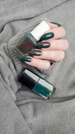 Female hand with long nails and a green manicure holds a bottle of nail polish
