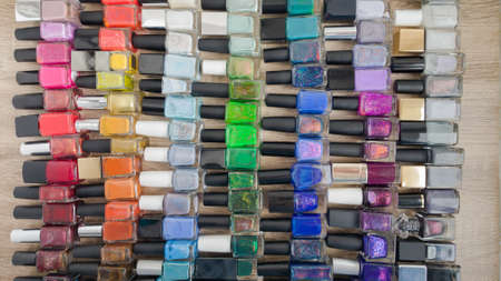 Background for design. A multi-colored bottles with nail polishes laid out on the wooden tableの写真素材