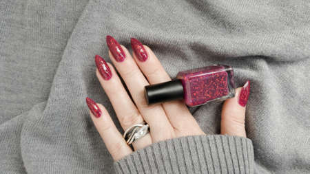 Female hand with long nails and a bottle of dark red nail polish