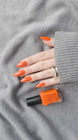 Female hand with long nails and orange ginger manicure holds a bottle of nail polish