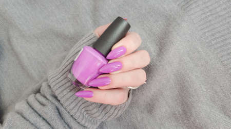 Woman hand with long nails manicure and pink bottle with nail polish