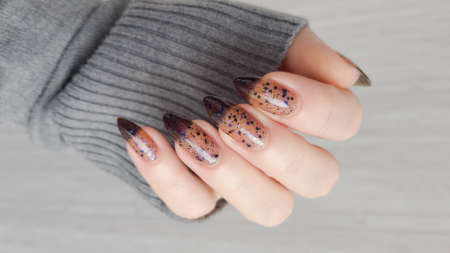 Female hand with long nails and black gray manicure holds a bottle of nail polish