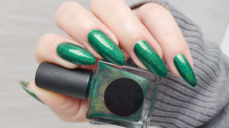 Female hand with long nails and a green manicure holds a bottle of nail polish