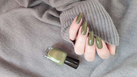 Female hand with long nails and a green manicure holds a bottle of nail polish