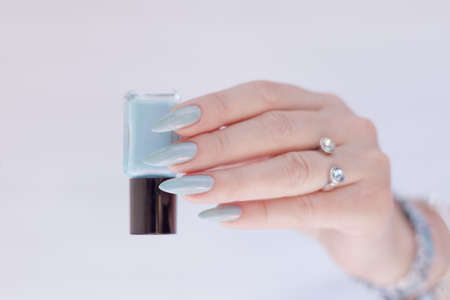 Female hand with long nails and light blue manicure with bottles of nail polishの写真素材