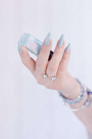 Female hand with long nails and light blue manicure with bottles of nail polishの写真素材