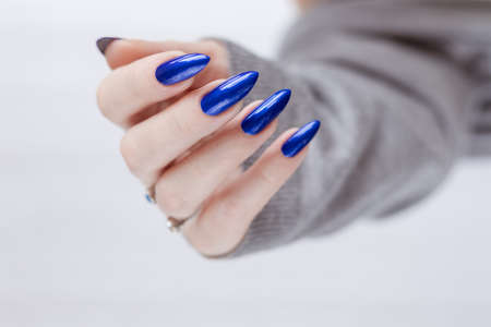 Female hand with long nails and blue manicure with bottles of nail polishの写真素材