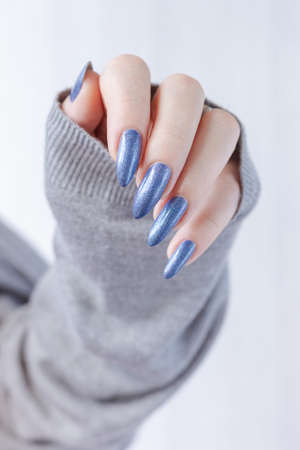 Female hand with long nails and light blue manicure with bottles of nail polishの写真素材