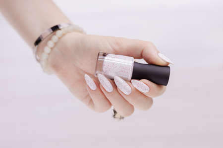 Female hand with long nails and a bottle of light white nail polish