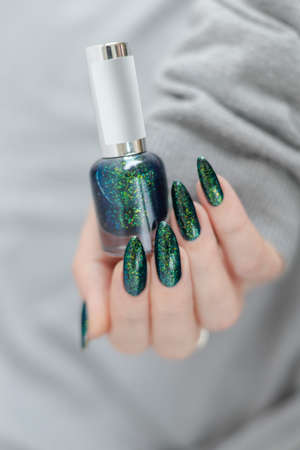 Female hand with long nails and a bottle of dark emerald green nail polish