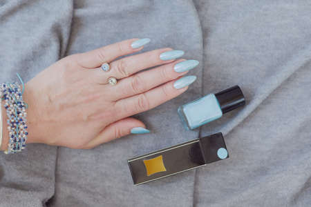 Female hand with long nails and light blue manicure with bottles of nail polish