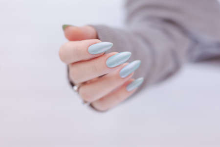 Female hand with long nails and light blue manicure with bottles of nail polishの写真素材