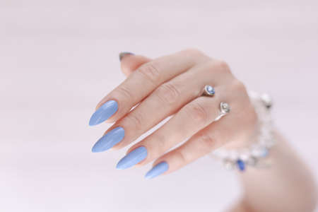 Female hand with long nails and light blue manicure with bottles of nail polish