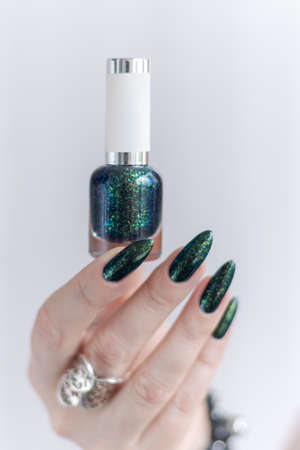 Female hand with long nails and a bottle of dark emerald green nail polishの写真素材