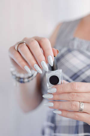 Female hand with long nails and light blue manicure with bottles of nail polishの写真素材