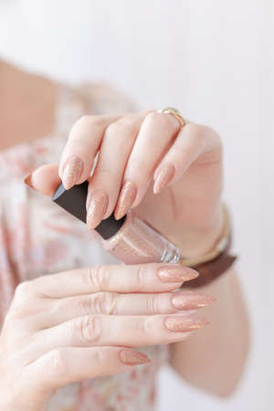 Female hand with long nails and a bottle of beige nude nail polish