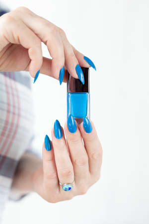 Female hand with long nails and blue manicure with bottles of nail polishの写真素材
