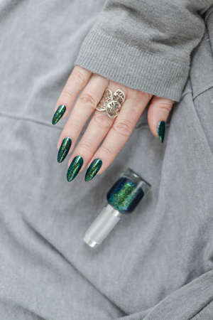 Female hand with long nails and a bottle of dark emerald green nail polish