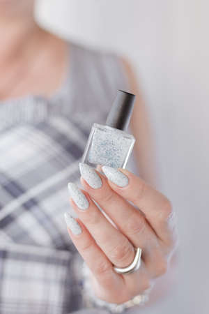 beautiful woman hands with long nails light white manicure and a bottle of nail polishの写真素材