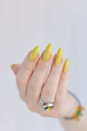 Female hand with long nails and a bottle of bright yellow green nail polishの写真素材
