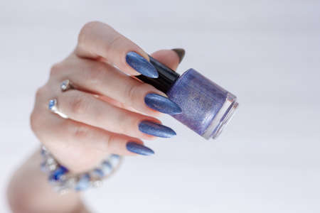 Female hand with long nails and blue manicure with bottles of nail polish